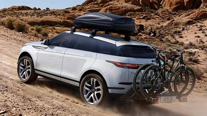 A Land Rover vehicle driving up a dusty hill with bikes attached to the boot